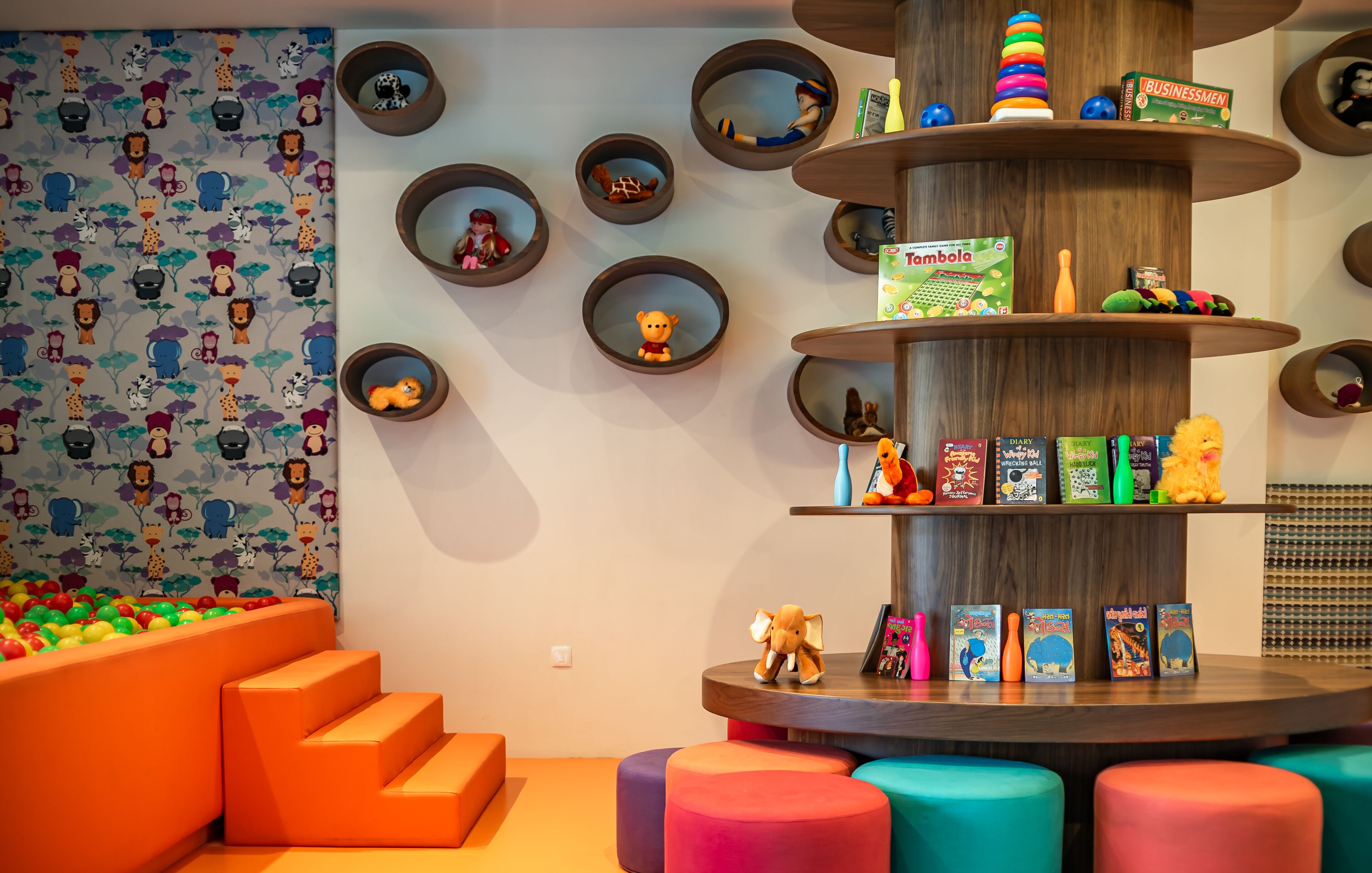 A children's play area with colorful seating, a ball pit, and shelves with toys and games.