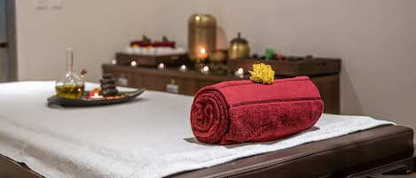 A massage table with a rolled towel and a bottle of oil.