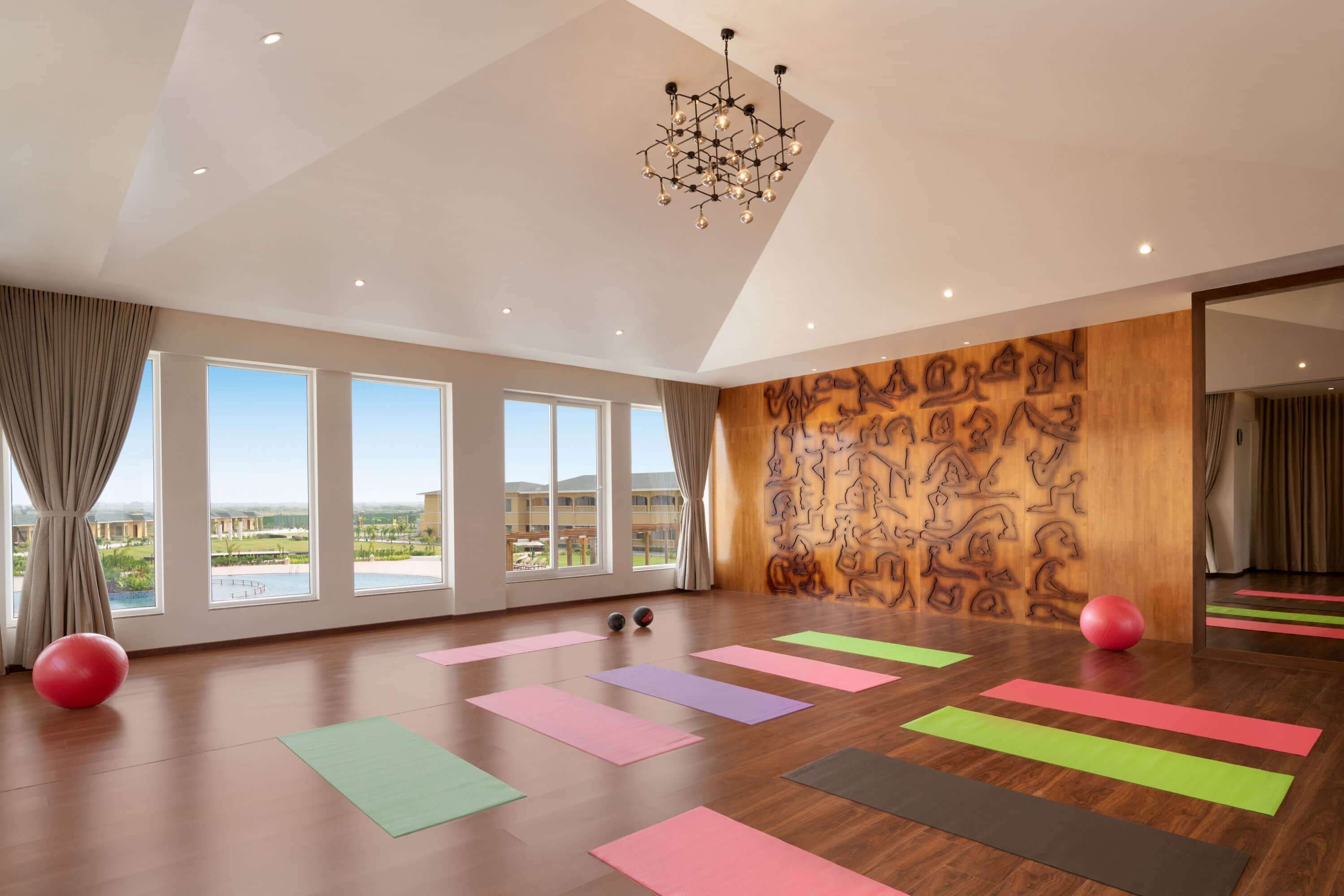 Ein geräumiges Zimmer mit großen Fenstern, Holzvertäfelung an den Wänden und Yogamatten.