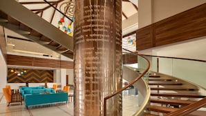 Un vestíbulo moderno con una escalera de caracol, un pilar central con inscripciones, un conjunto de sofás azules y una pared con diseño de chevron.