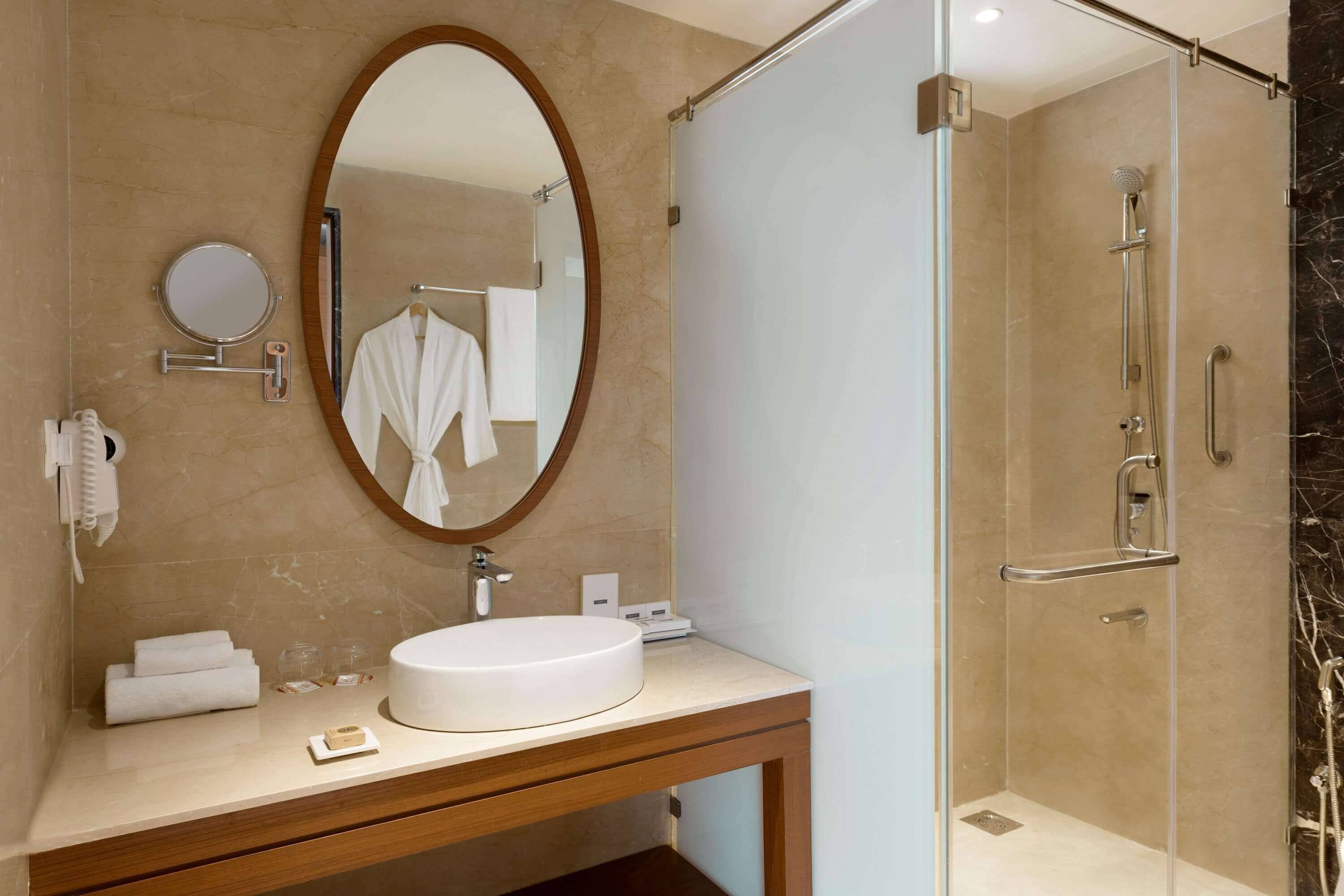 Un baño moderno con un espejo redondo, un lavamanos circular y una ducha con mampara de vidrio.