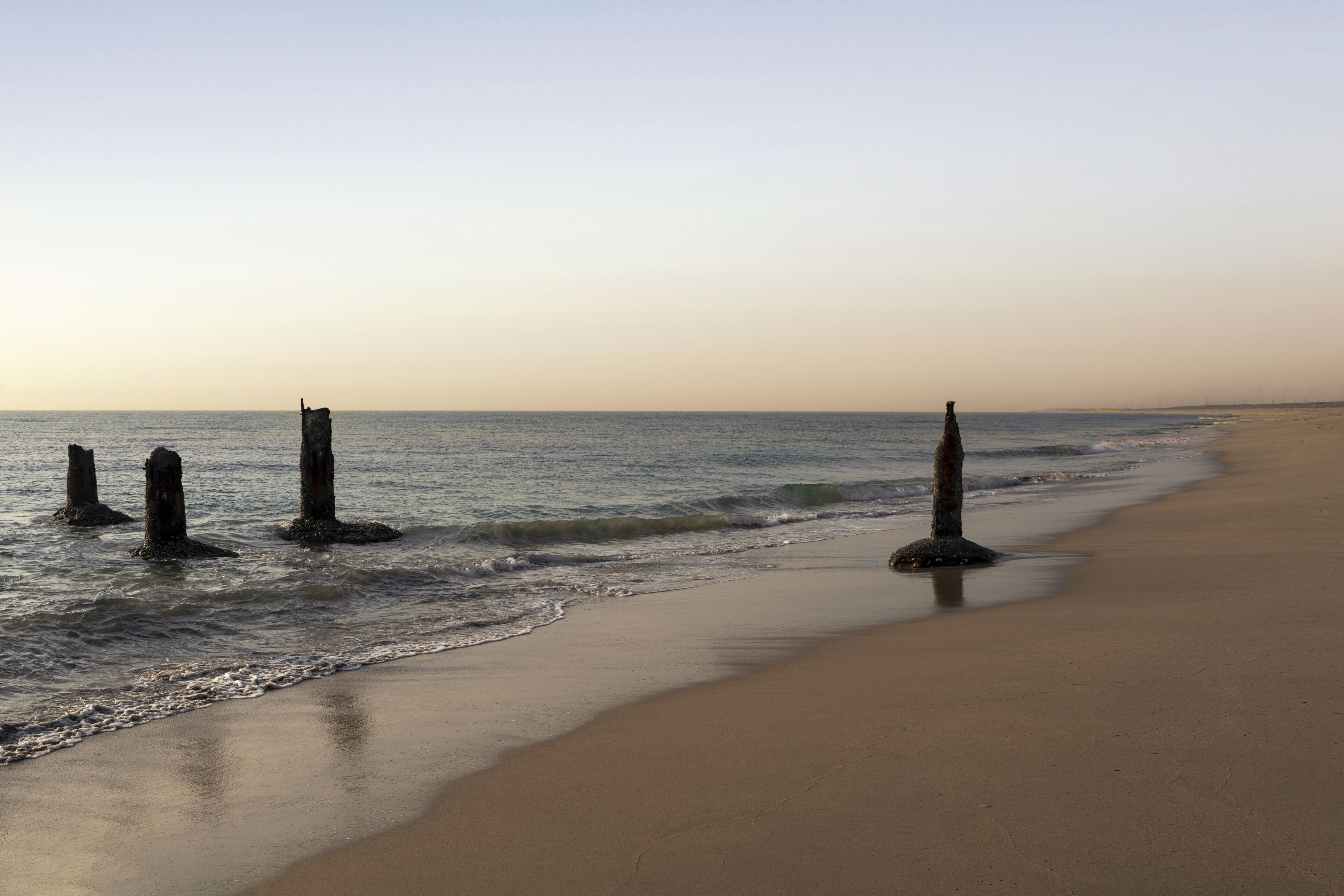 Une plage avec un rivage sablonneux et plusieurs structures verticales dans l’eau.