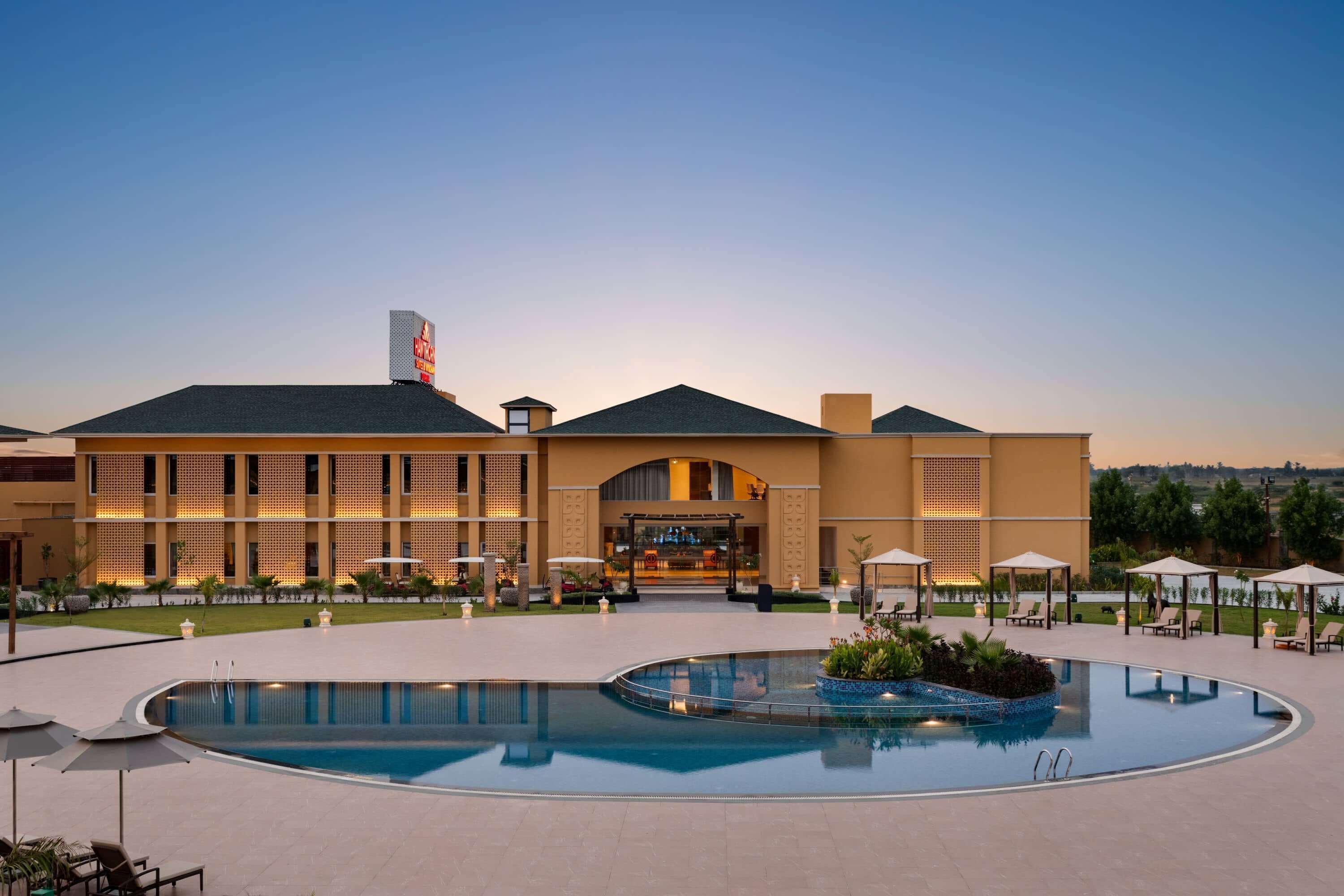 Un hotel con piscina, mobiliario exterior y una entrada bien iluminada.
