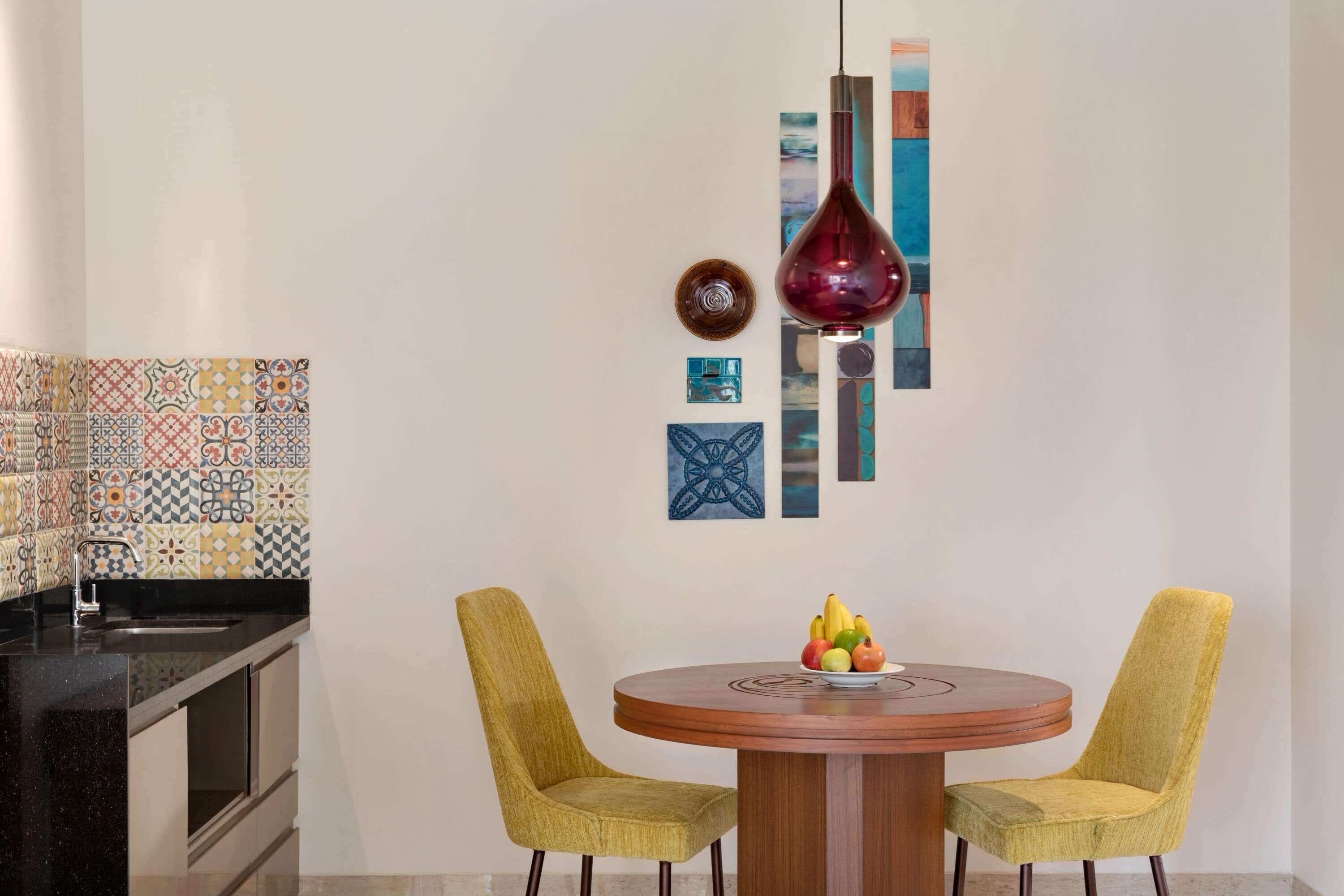 A kitchen with a patterned backsplash, a round wooden table with two yellow chairs, and a hanging pendant light.
