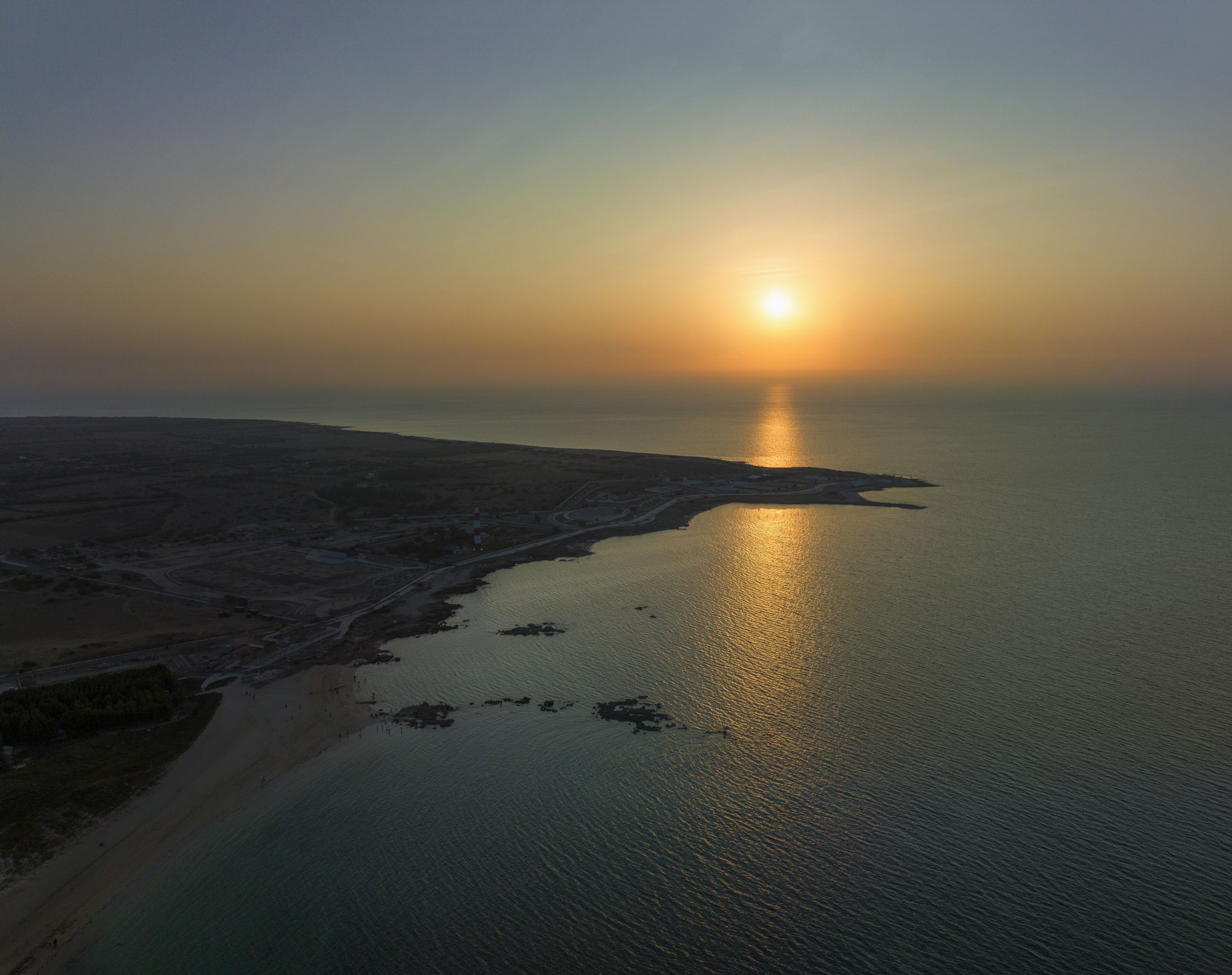 An aerial view of a coastal area with a beach and a body of water reflecting the sun.