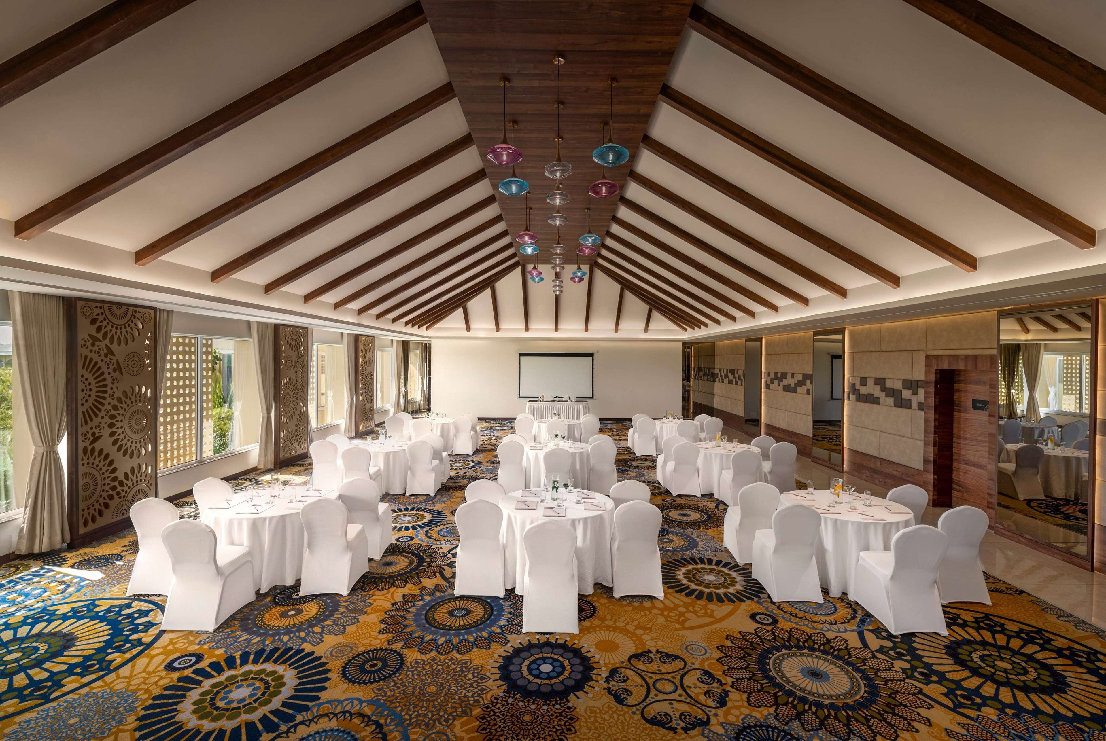 A conference room with round tables, white chairs, and a patterned carpet.