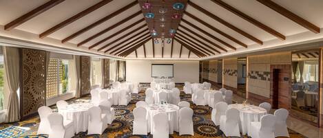 A conference room with round tables, white chairs, and a patterned carpet.