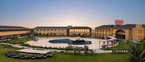 Un patio de hotel con piscina central, mobiliario exterior y un edificio grande con un letrero.