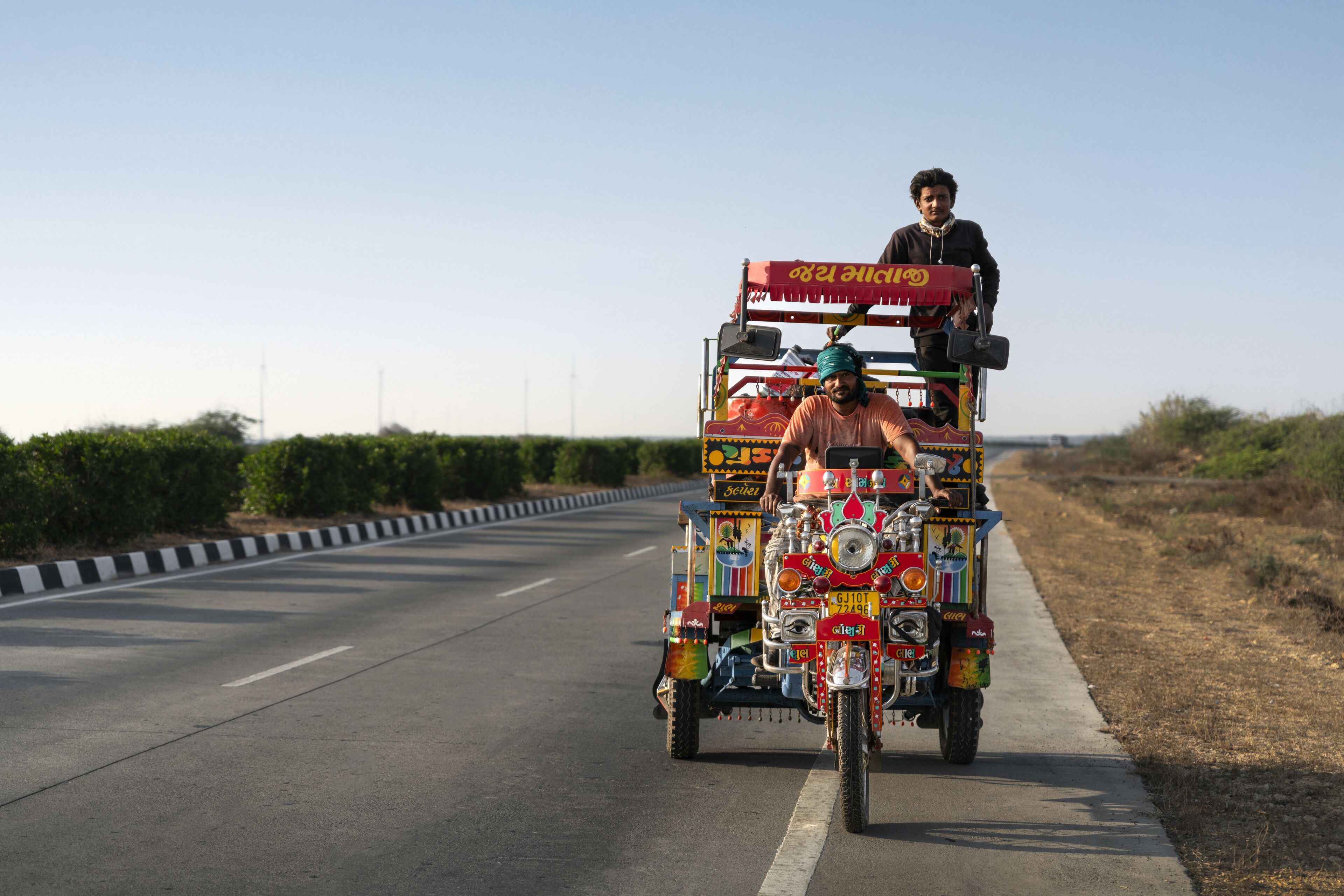 A colorful rickshaw with multiple passengers and a driver on a road.