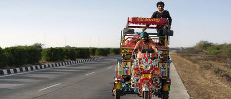 A colorful rickshaw with multiple passengers and a driver on a road.