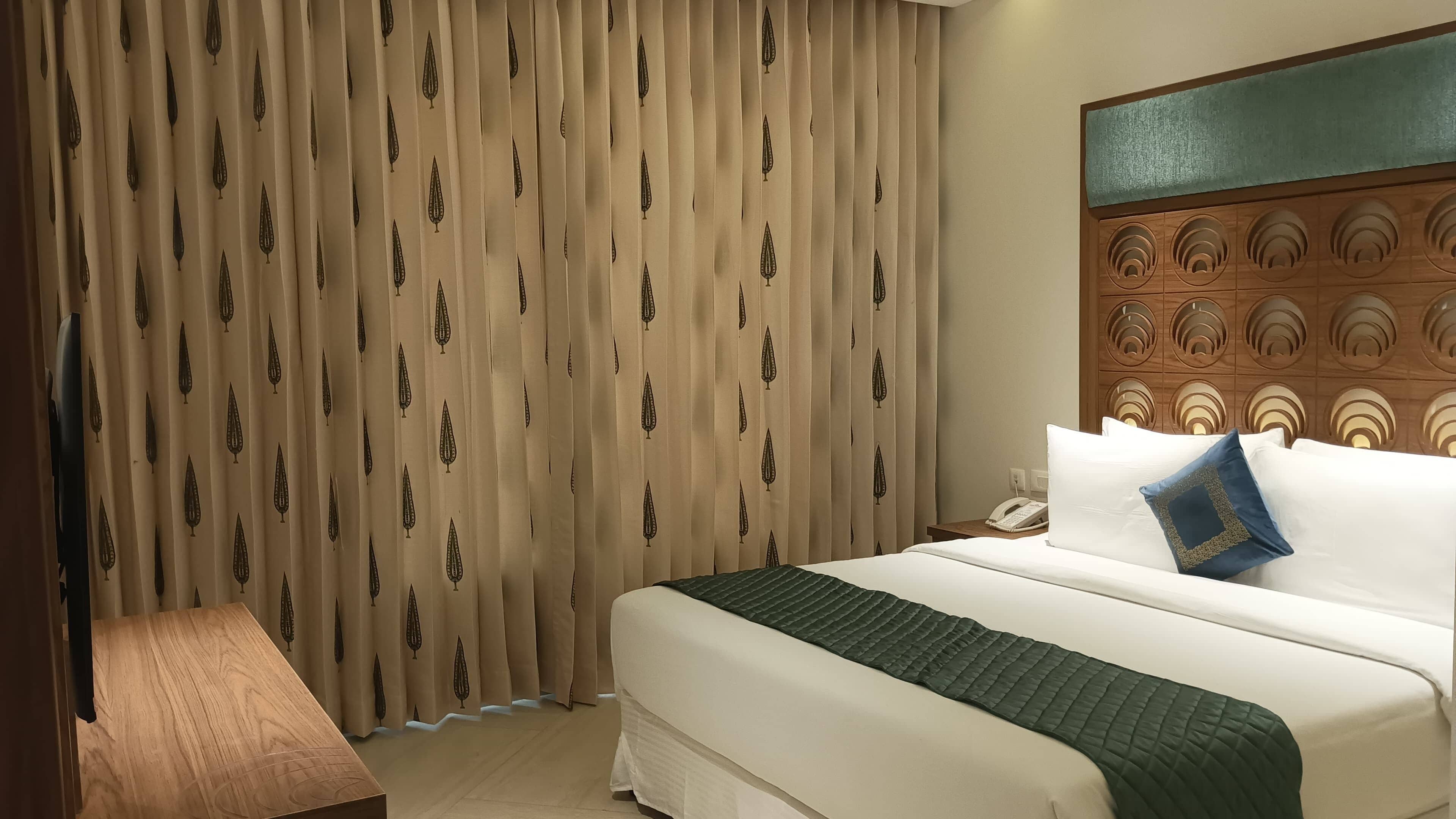A hotel room with a bed, a nightstand, a telephone, and a wall with a decorative panel.