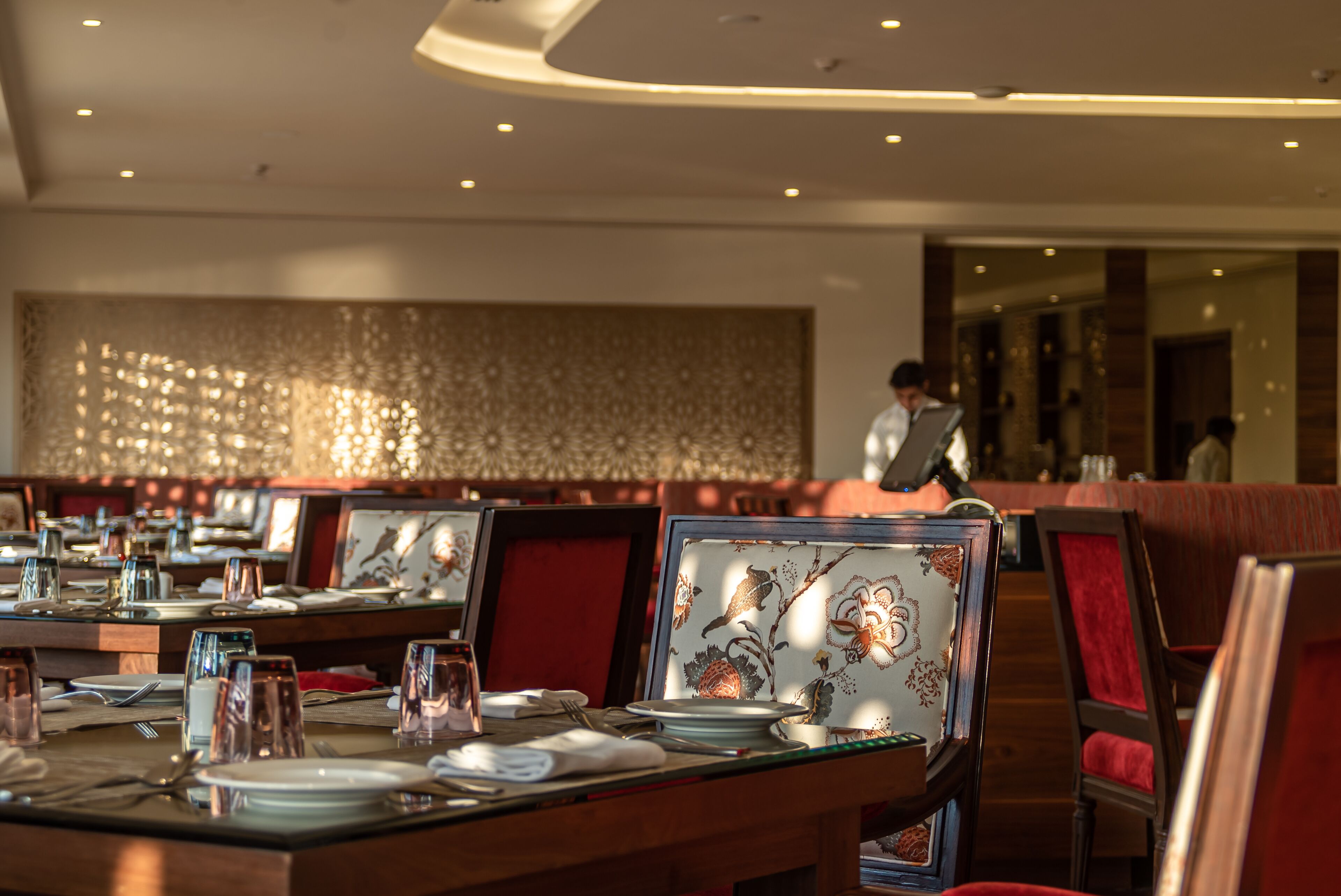 Un restaurante con mesas dispuestas para comer, con manteles estampados y sillas tapizadas en rojo.