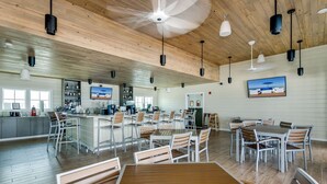 Ein geräumiger Essbereich mit Holztischen und -stühlen, eine Bar mit Fernseher sowie ein Deckenventilator.