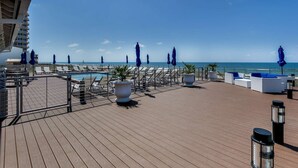 Ein Poolbereich auf dem Dach mit Liegestühlen, Sonnenschirmen und Blick auf den Ozean.