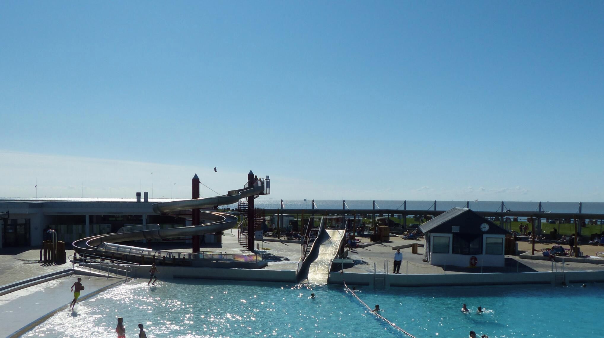 Ein Schwimmbecken mit Wasserrutsche und Rettungsschwimmerstation.