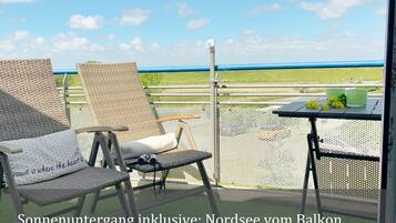 Ein Balkon mit Korbstühlen und einem Tisch, mit Blick auf eine grüne Landschaft.