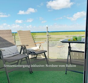 Ein Balkon mit Korbstühlen und einem Tisch, mit Blick auf eine grüne Landschaft.