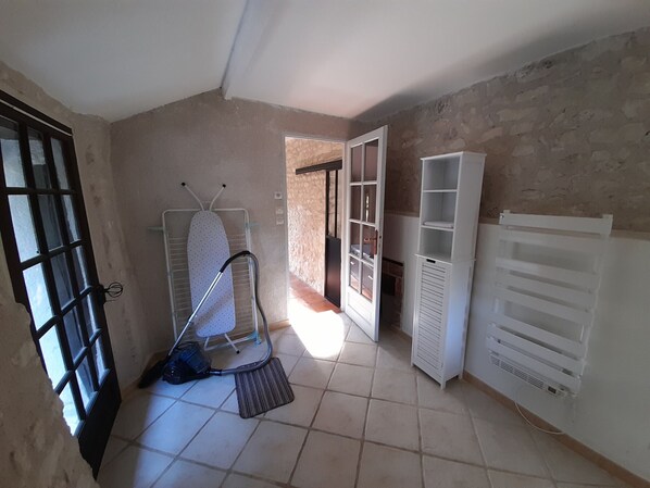 A room with a tiled floor, a standing heater, an ironing board, and a door leading to another room.