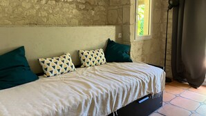 A room with a stone wall, a bed with patterned pillows, a window with a view, and a curtain. - Charming House with Terrace & Garden, Near La Roche-Posay Town Center (La Roche-Posay)