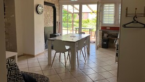 A room with a dining table, chairs, a clock, a stove, and a view of the outdoors. - Charming House with Terrace & Garden, Near La Roche-Posay Town Center (La Roche-Posay)