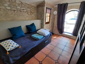A room with a bed, a window with curtains, a stone wall, and a tiled floor.