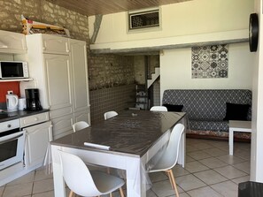 A compact kitchen with a dining table, chairs, a microwave, a coffee maker, and a patterned sofa.