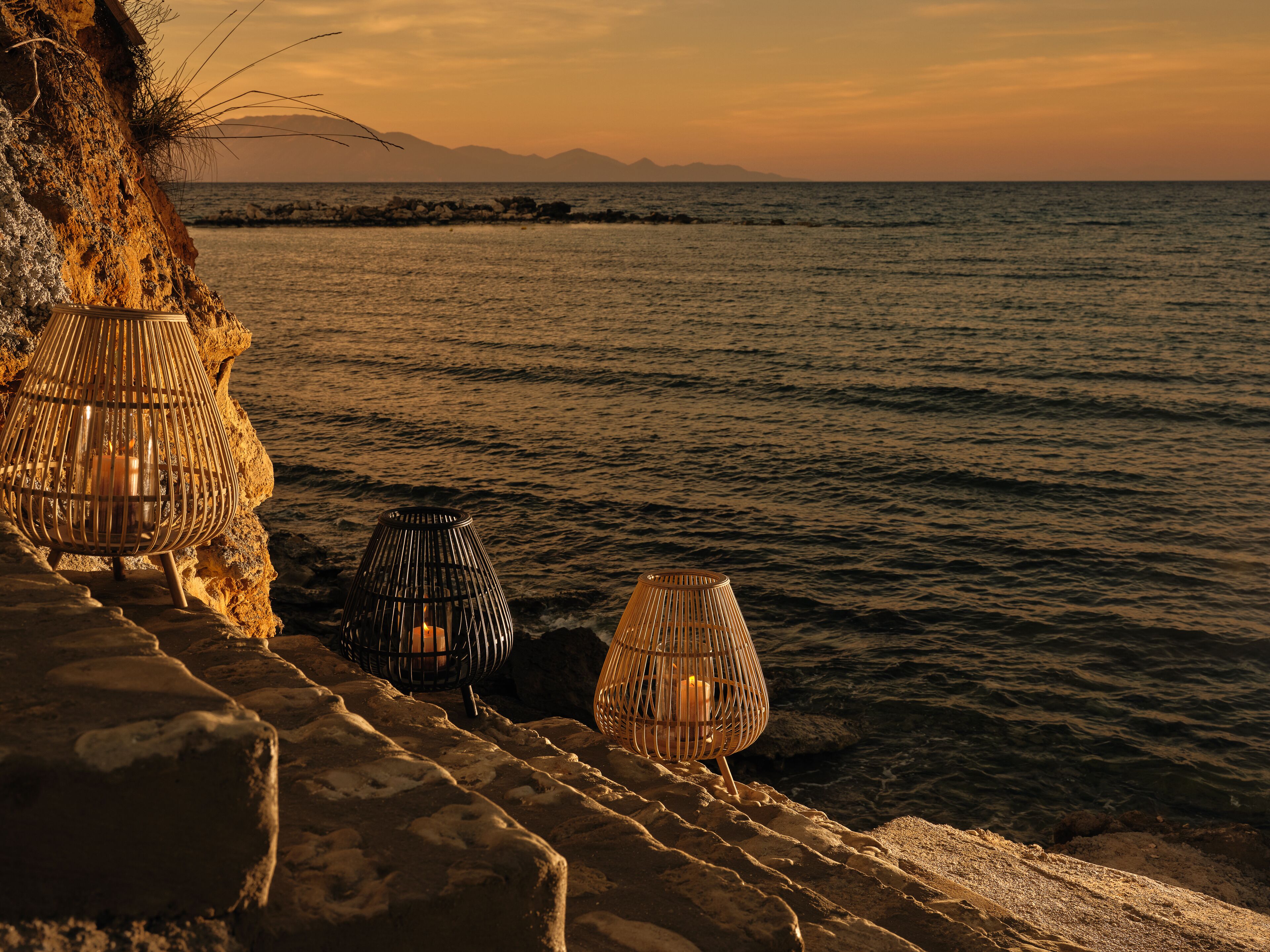Une scène de plage avec trois lanternes en osier placées sur une corniche en pierre surplombant la mer.
