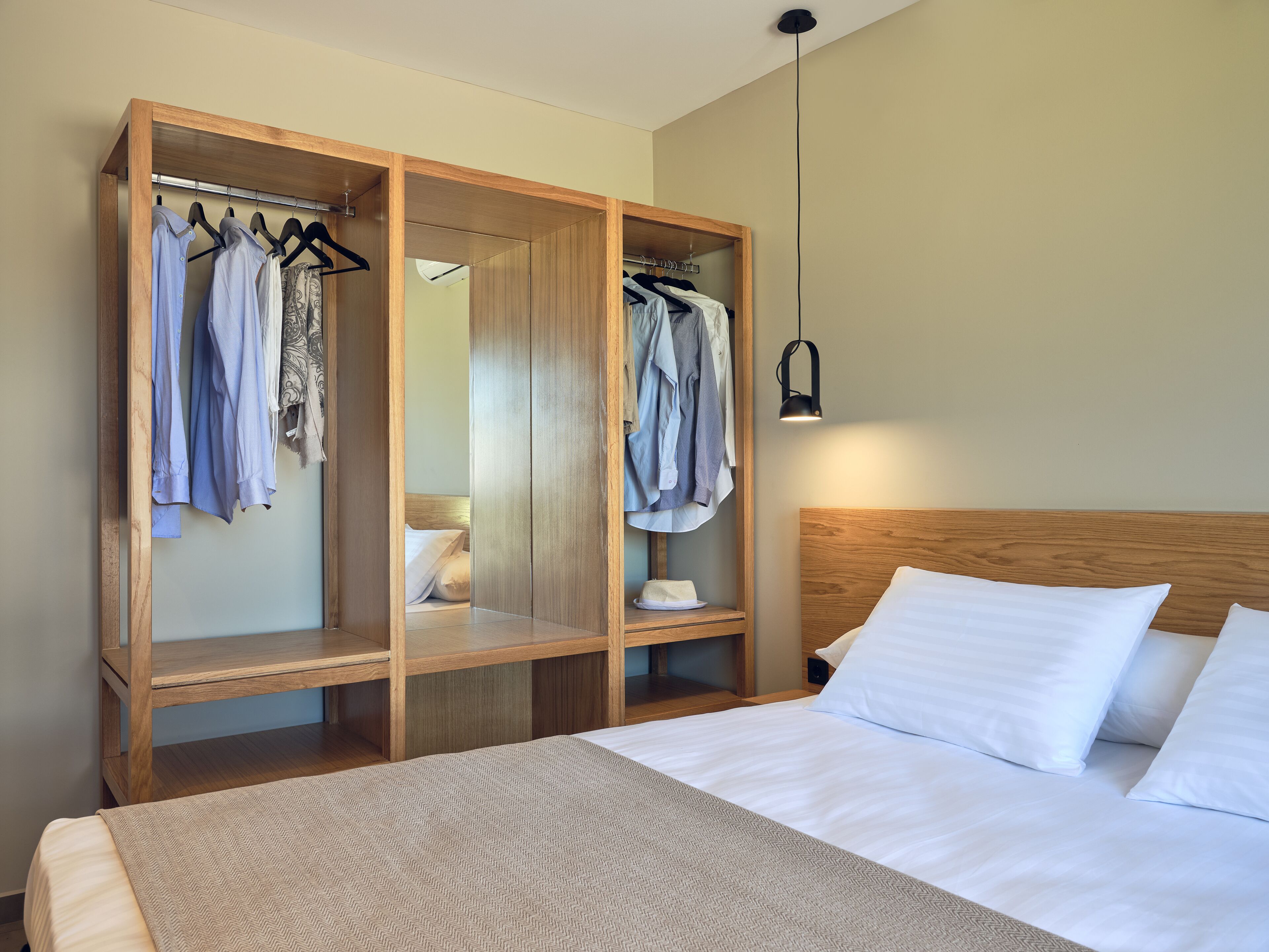 Una habitación de hotel con un armario de madera, una cama con ropa blanca y una mesita de noche con lámpara.
