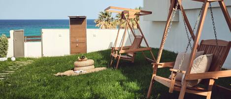 A wooden swing set and a chair in a grassy outdoor area with a view of the ocean.