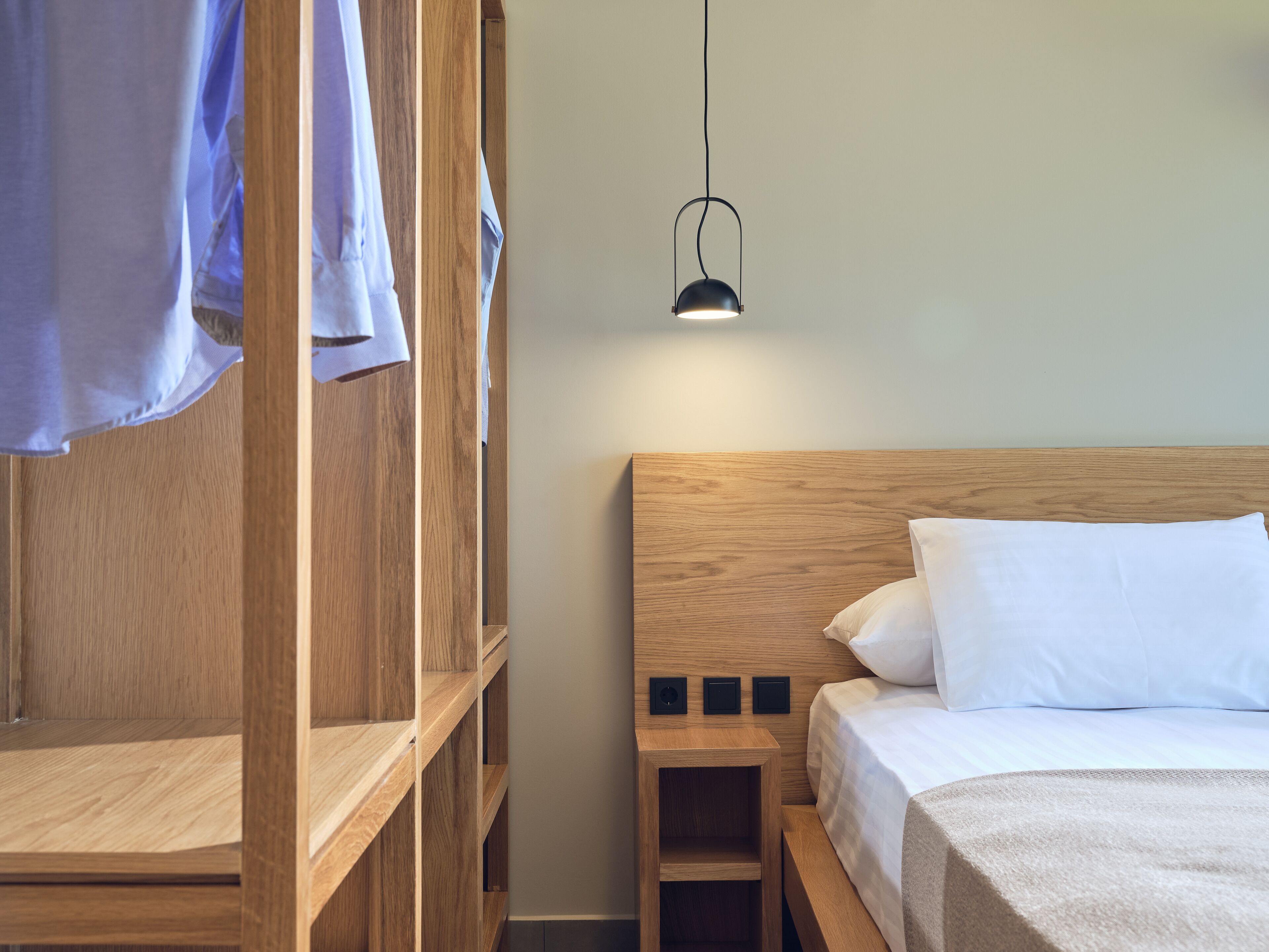 A neatly arranged bedroom with a wooden headboard, a single bed with white bedding, and a small bedside table.
