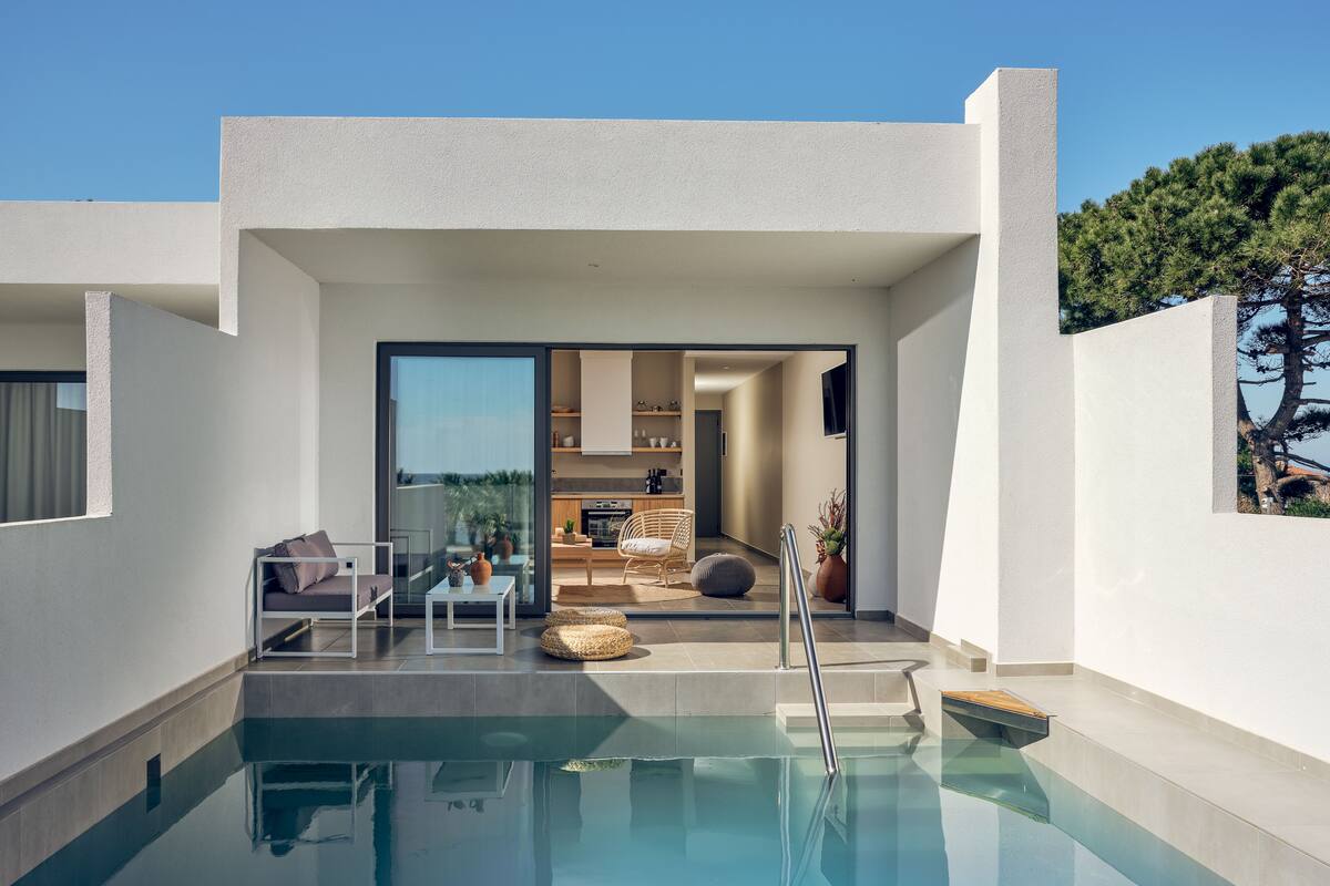 Un área de piscina moderna con un porche acristalado, un comedor y una cocina visible a través de puertas de vidrio.