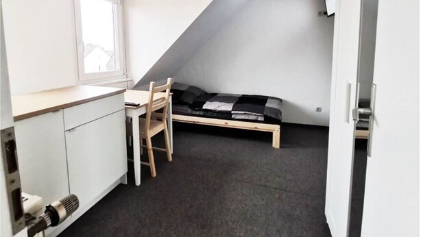 A small, compact room with a kitchenette, a single bed, and a window. - Apartment Hainstädter Straße (Hanau)
