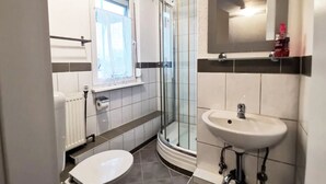 A compact bathroom with a toilet, a sink, a glass shower enclosure, and a window. - Apartment Hainstädter Straße (Hanau)