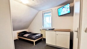 A small, compact room with a single bed, a desk, and a television mounted on the wall. - Apartment Hainstädter Straße (Hanau)