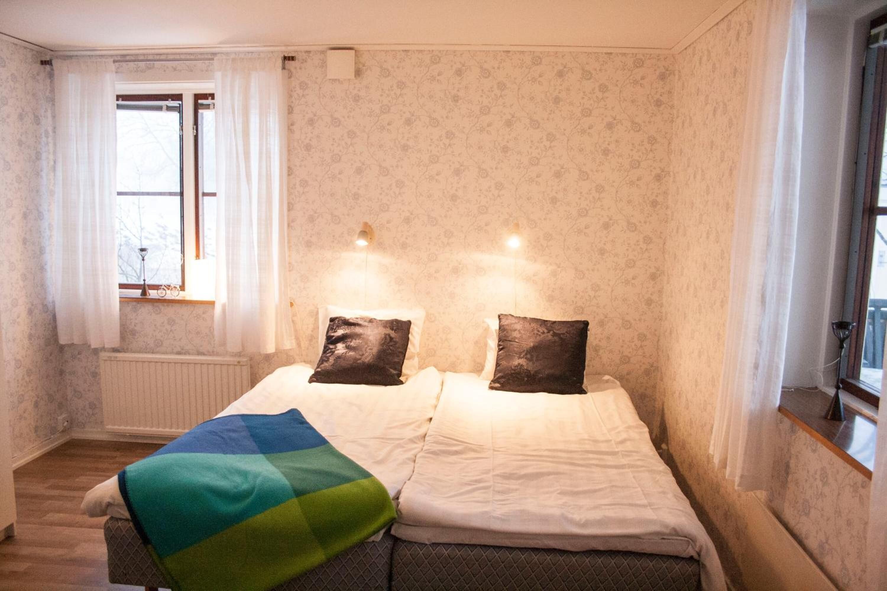 A bedroom with two beds, a radiator, and a window with curtains.