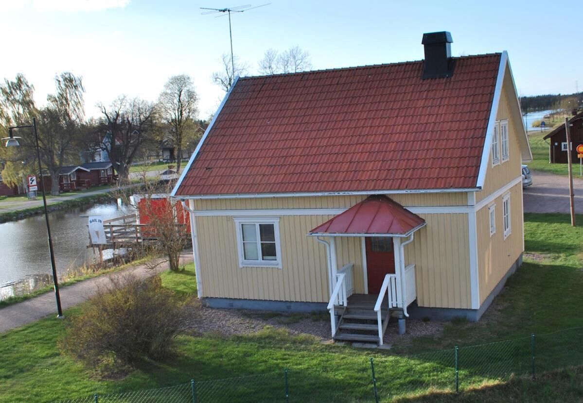 A two-story house with a red roof, a small porch, and a view of a river.