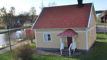 A two-story house with a red roof, a small porch, and a view of a river.