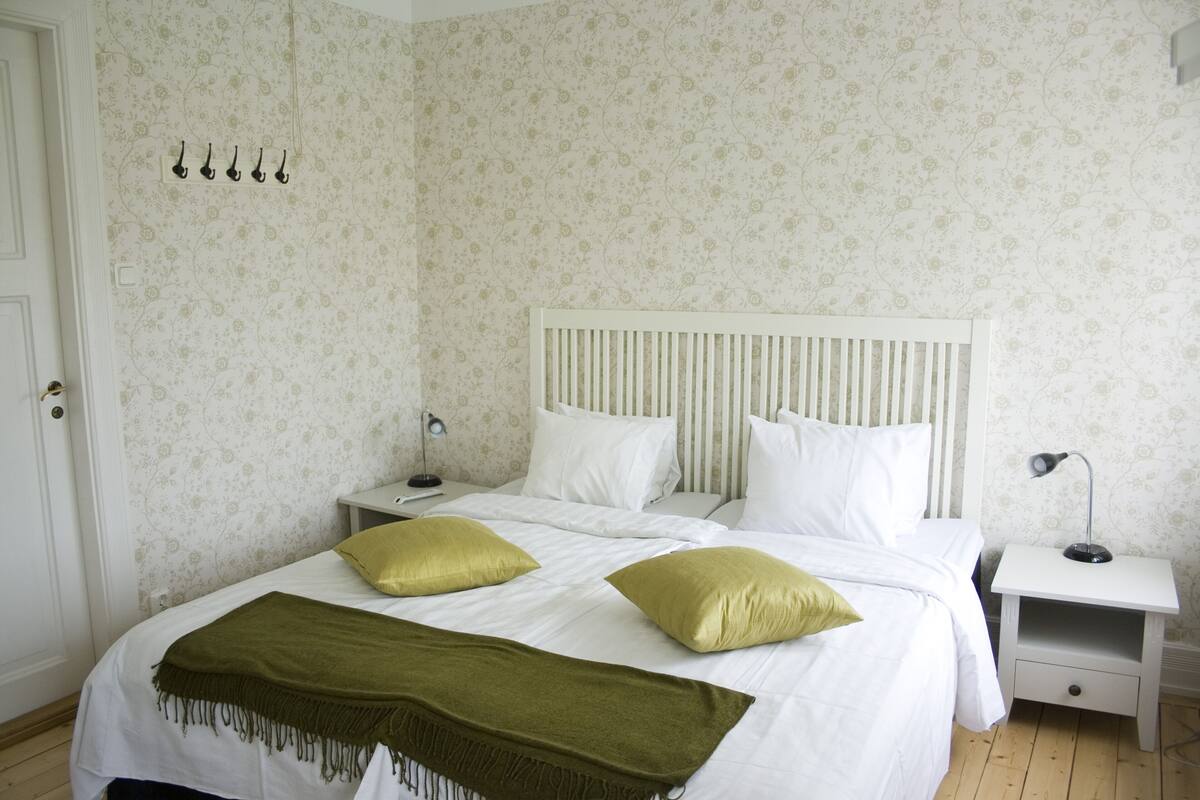 Ein Schlafzimmer mit einem Bett, zwei Nachttischen, einer Stehlampe und einer Tür.