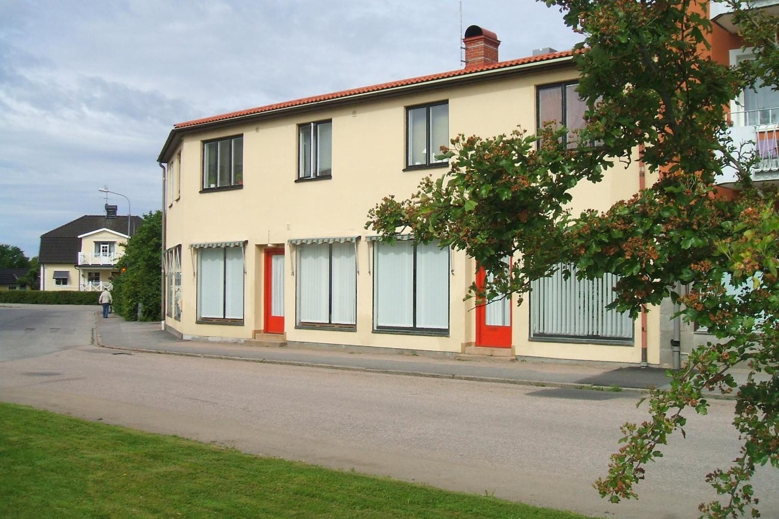 A two-story building with a red door and windows, a paved street, and a person walking in the distance.