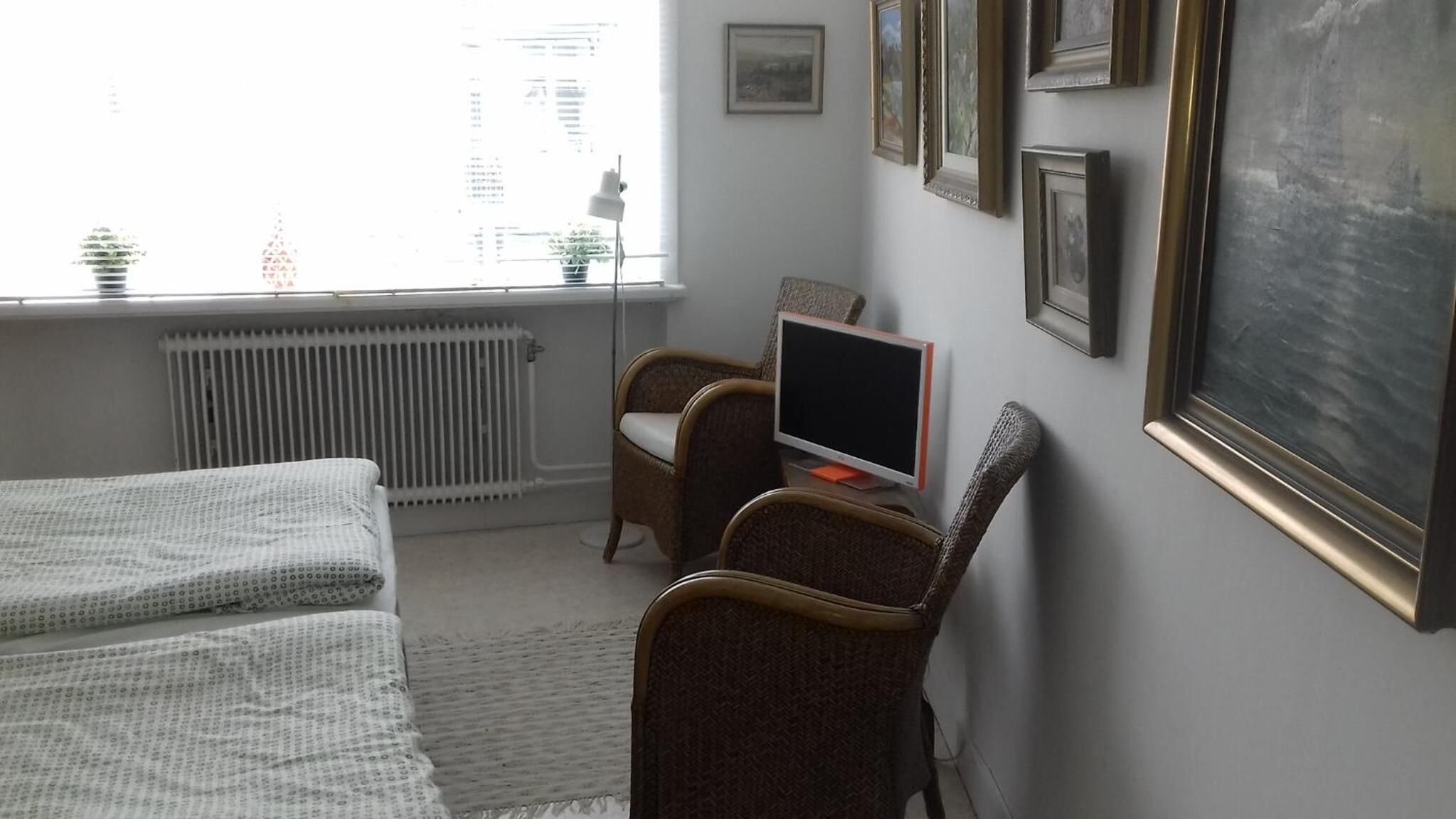 Une chambre avec deux lits, un bureau avec un ordinateur et des tableaux encadrés accrochés au mur.