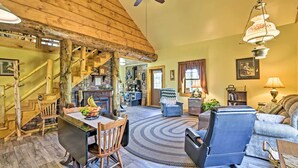 A spacious living room with a wooden staircase, a dining area with a table and chairs, and a kitchen in the background.