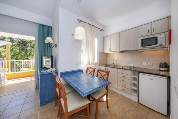 A compact kitchen with a dining table and chairs, a microwave, a sink, and a small refrigerator. - Comitas Isla del Aire (Sant Lluis)