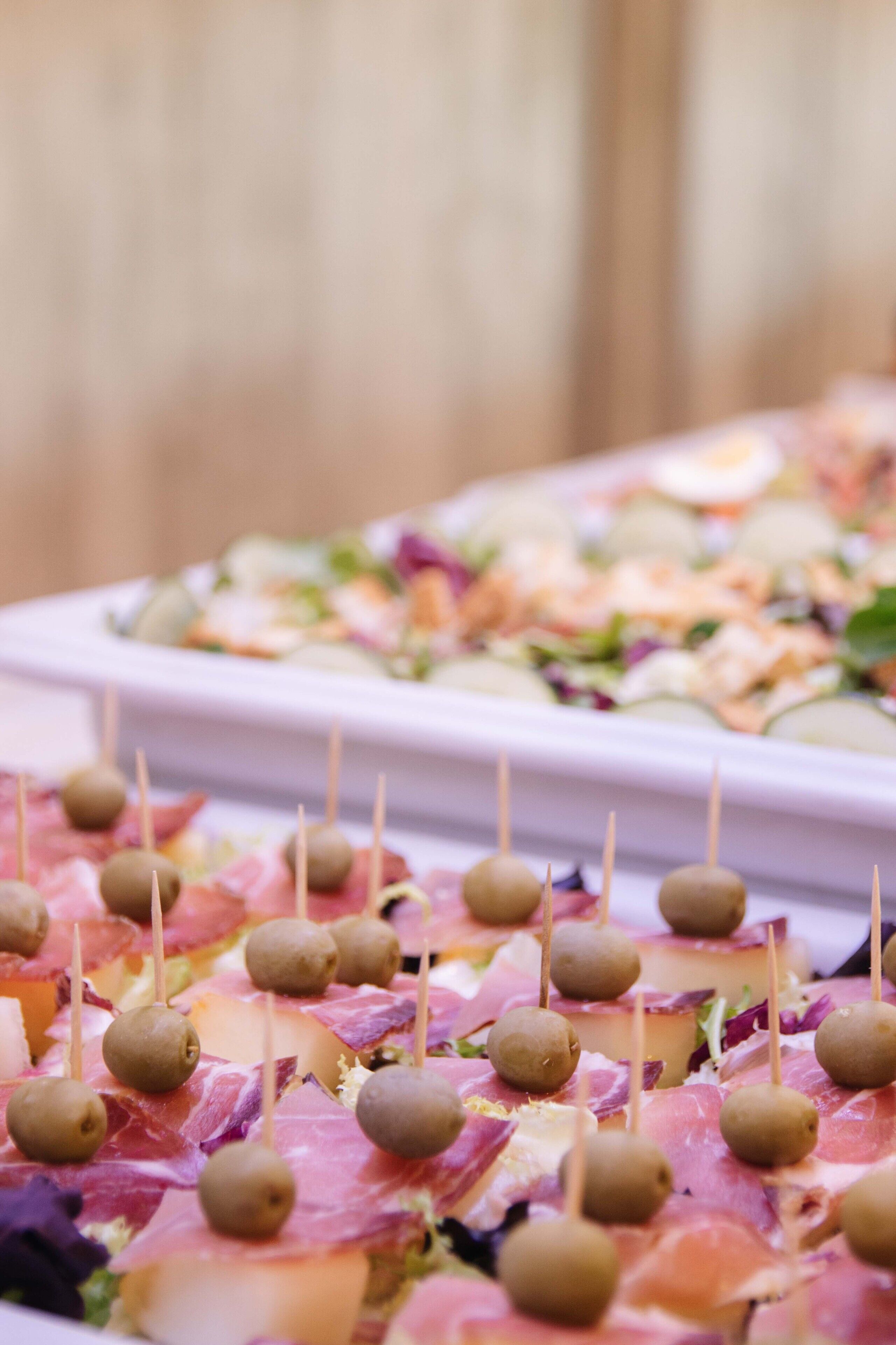 A platter of appetizers with skewered olives and meat slices.
