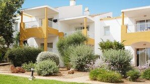 Un hôtel à plusieurs étages doté de balcons, d’un jardin agrémenté de divers arbustes et de fleurs, et surplombant un ciel d’un bleu limpide.