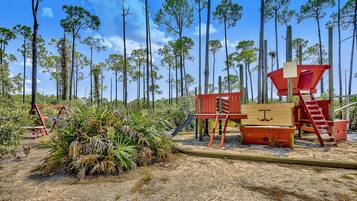 Kids can play on the playground's slide and climbing structure amidst the surrounding pine trees.