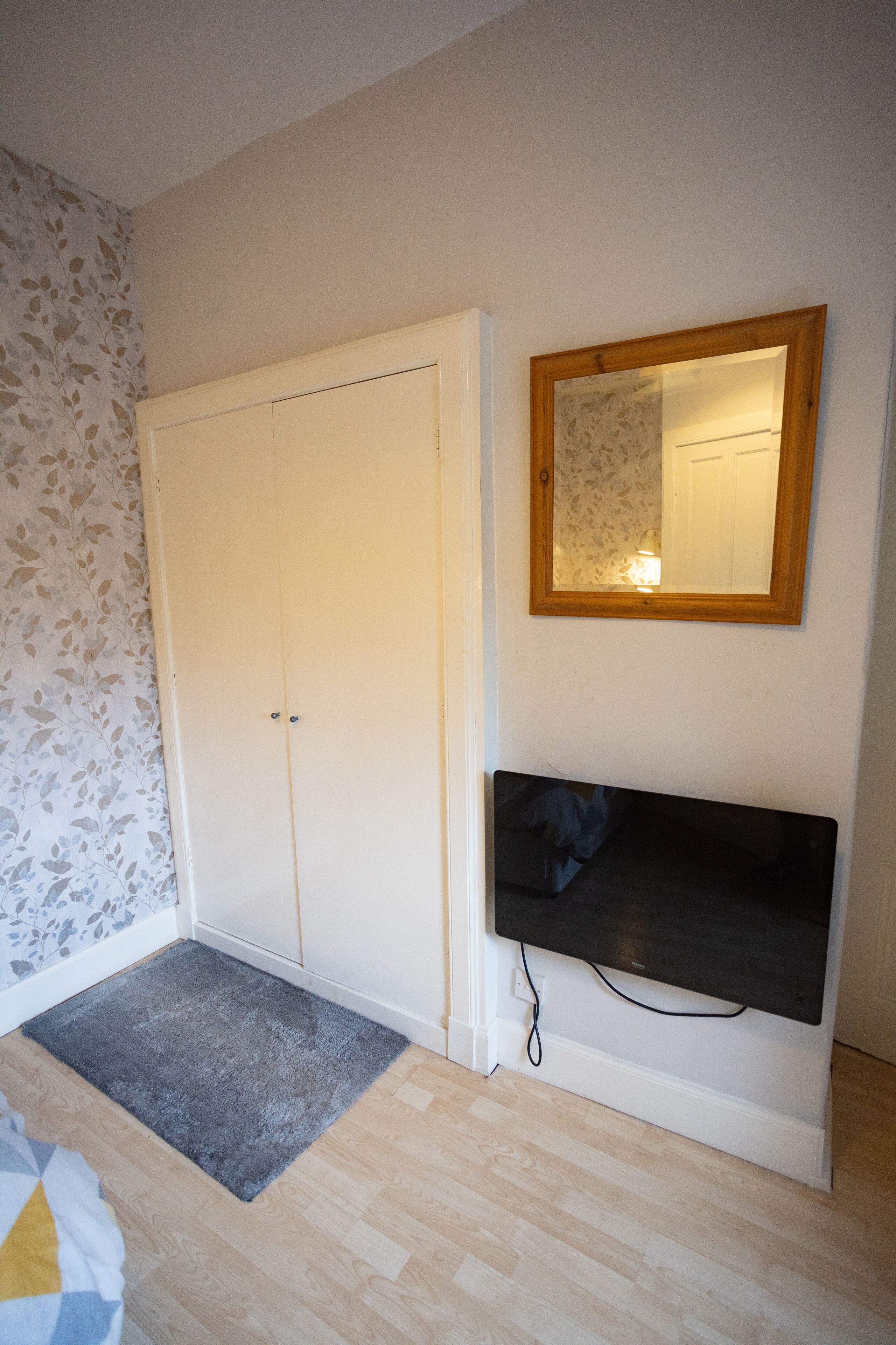 Et værelse med et hvidt skab, et spejl med træramme og et ophængt fjernsyn.