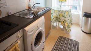 A compact kitchen with a washing machine, a sink, and a window with a view. - Sandgate 2-bed Apartment in Ayr Central Location (Ayr)