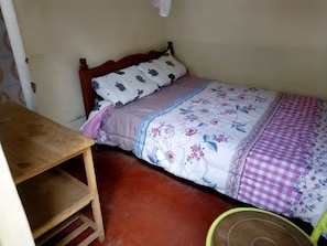 A small, single-bed room with a wooden bed frame, a wooden nightstand, and a green chair. - Comfort Motel (Nakuru)