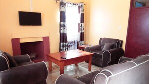 A living room with a fireplace, a television mounted on the wall, and two sofas. - Eastward Garden Hotel (Nyahururu)