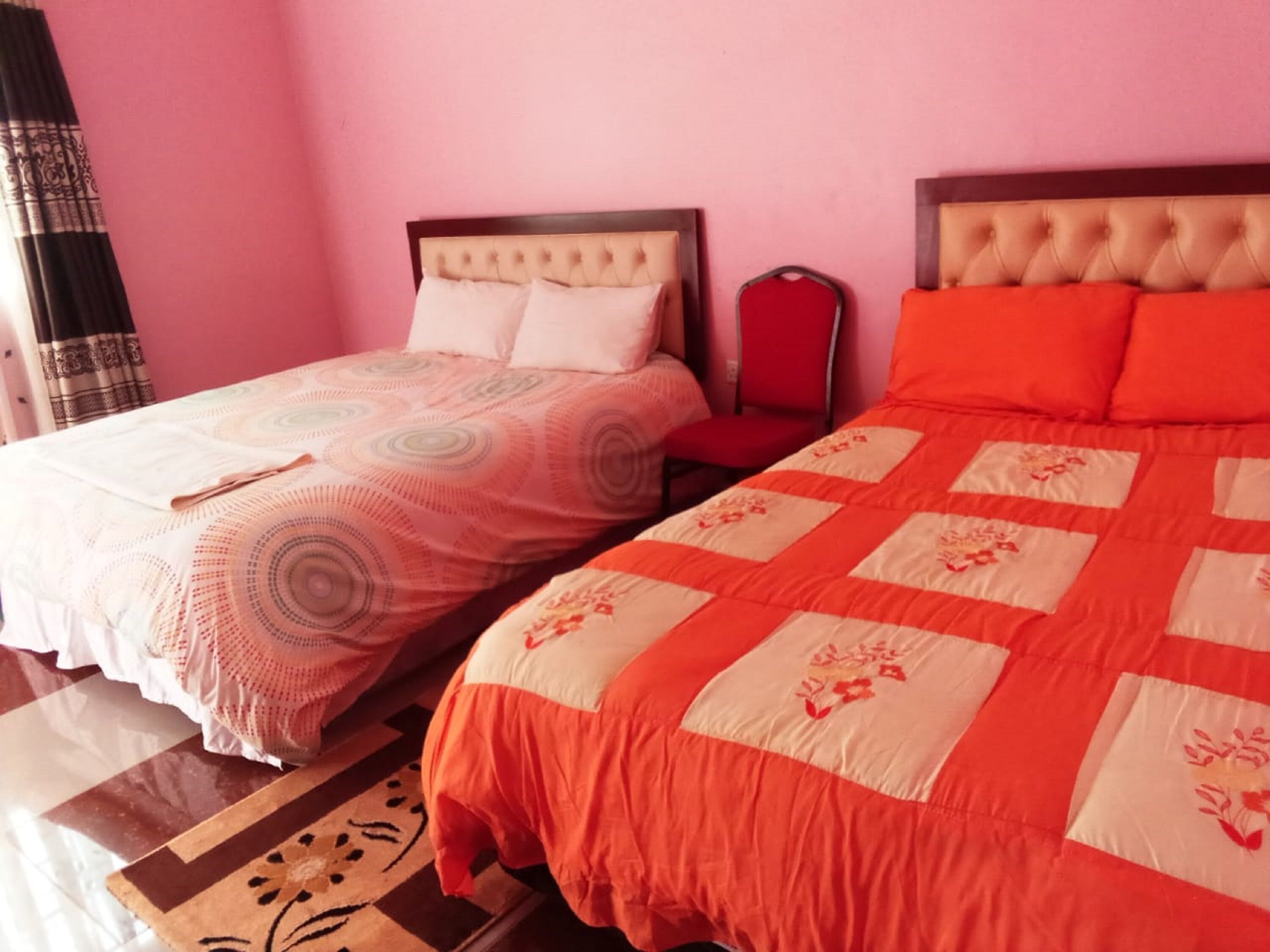 Two beds with different bedding styles in a room with pink walls and a patterned rug.